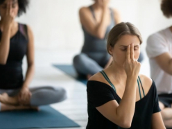 Gruppe sitzt im Schneidersitz auf Yogamatten und praktiziert Atemuebung mit geschlossenen Augen.