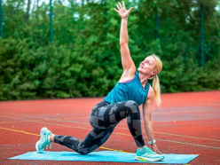 Sportlerin in grün schwarzem Trainingsoutfit bei Drehhaltung auf Yogamatte auf der Tartanbahn.