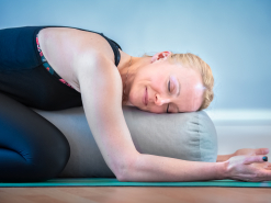 Frau in einer Yin-Yoga-Haltung, die über ein großes Yogakissen gebeugt liegt.